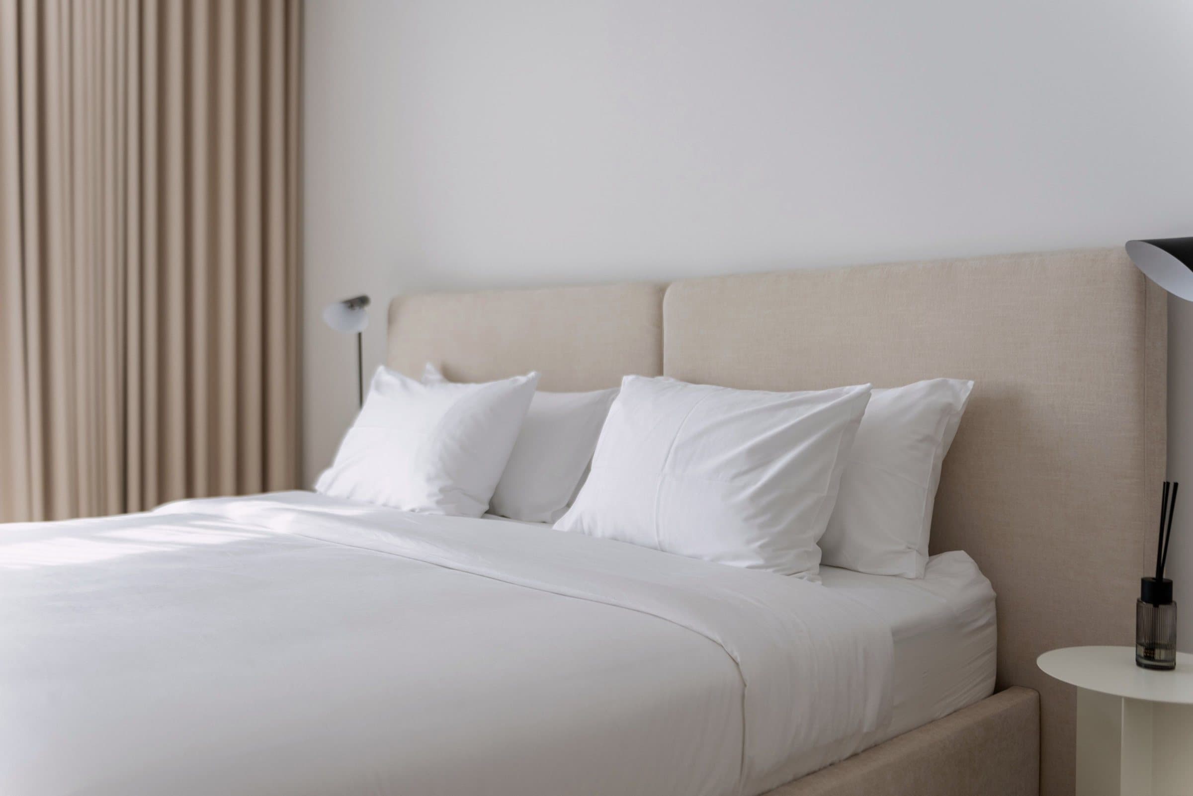 A modern bedroom in neutral tones, with a padded headboard and linen curtains. Illustration, not a client’s room.